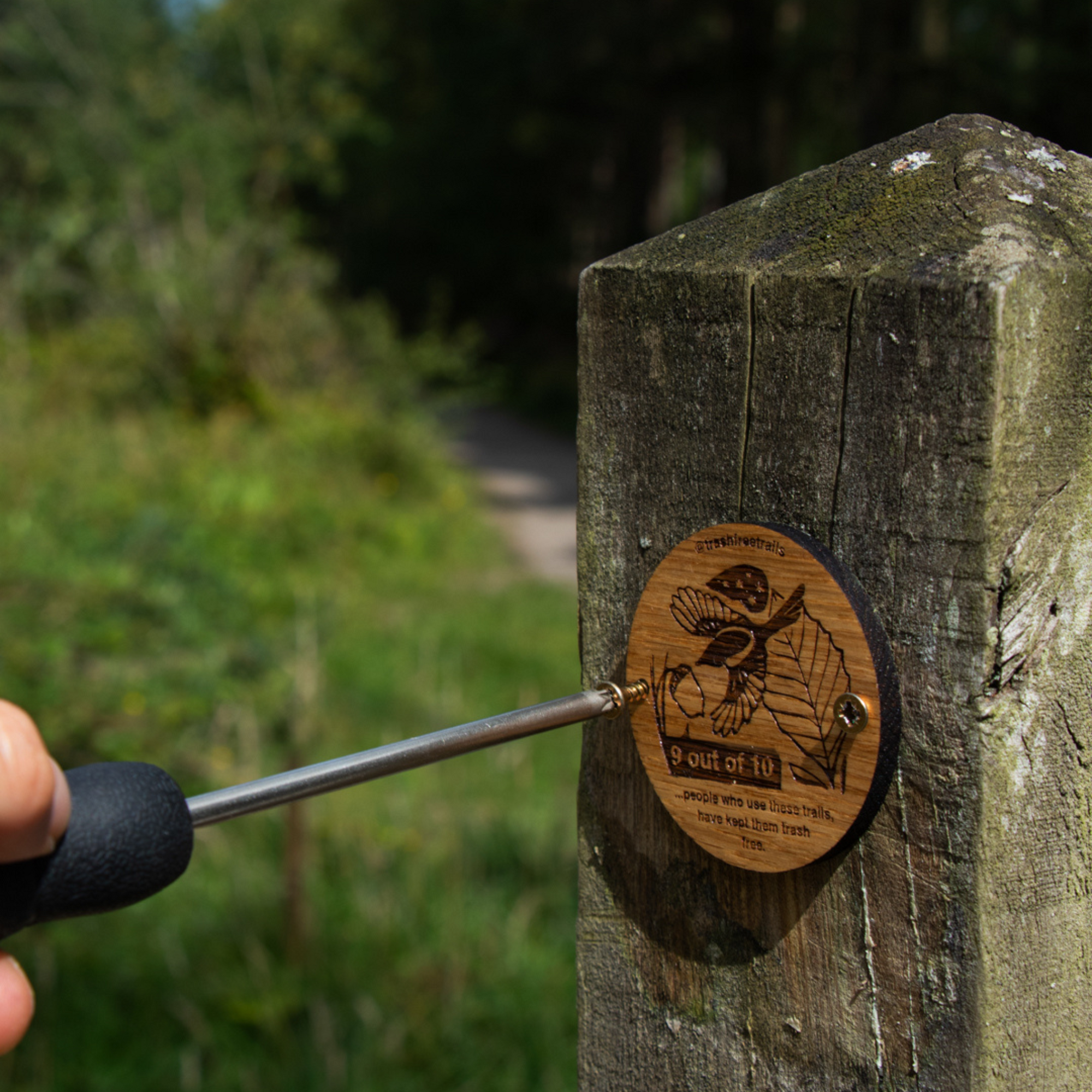 Wooden Waymarker with writing on Wooden Post  with a hand attaching it with a screwdriver.