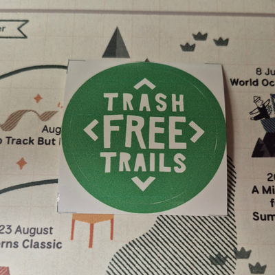 Green 'Trash Free Trails' sticker on a paper background