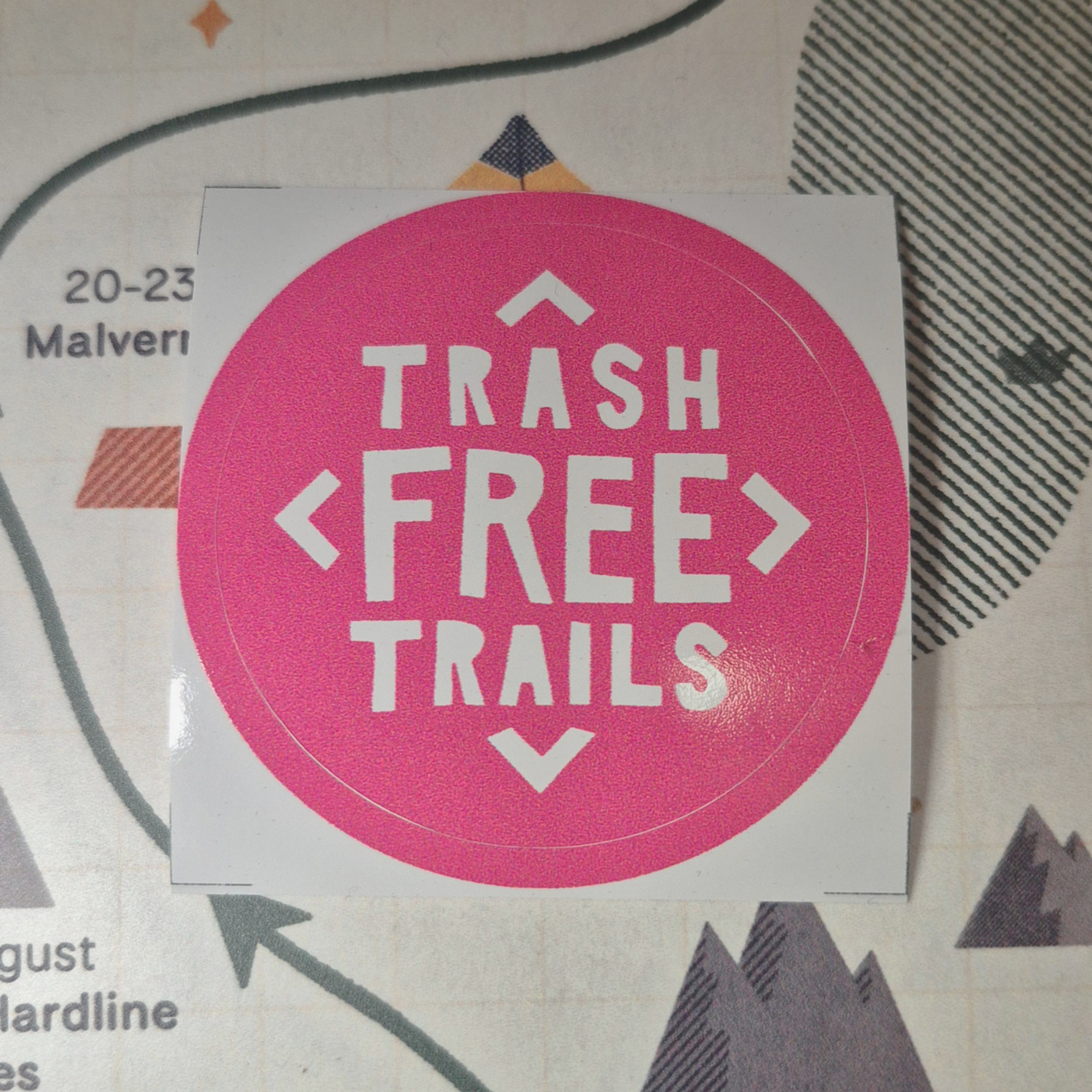Pink and white 'Trash Free Trails' sticker on a map background