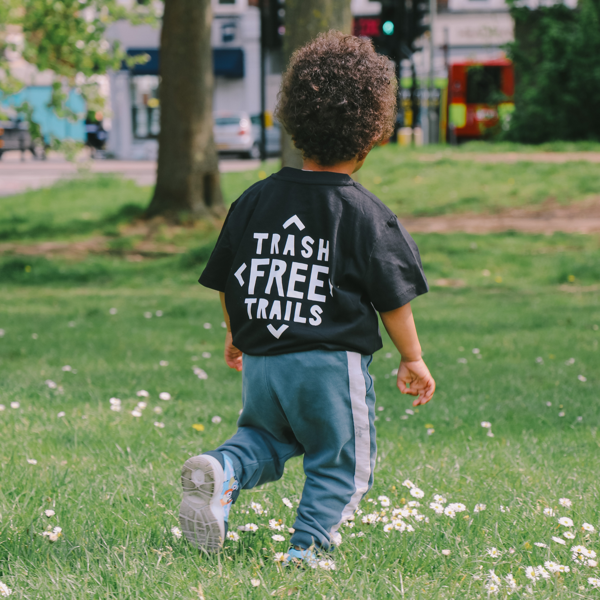 A child walking away with the black Trash Free Trails Tshirt on, showing the Trash Free Logo on the reverse.