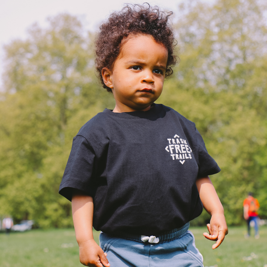 A child wearing a  Trash Free Trails Tshirt with some trees behind.  