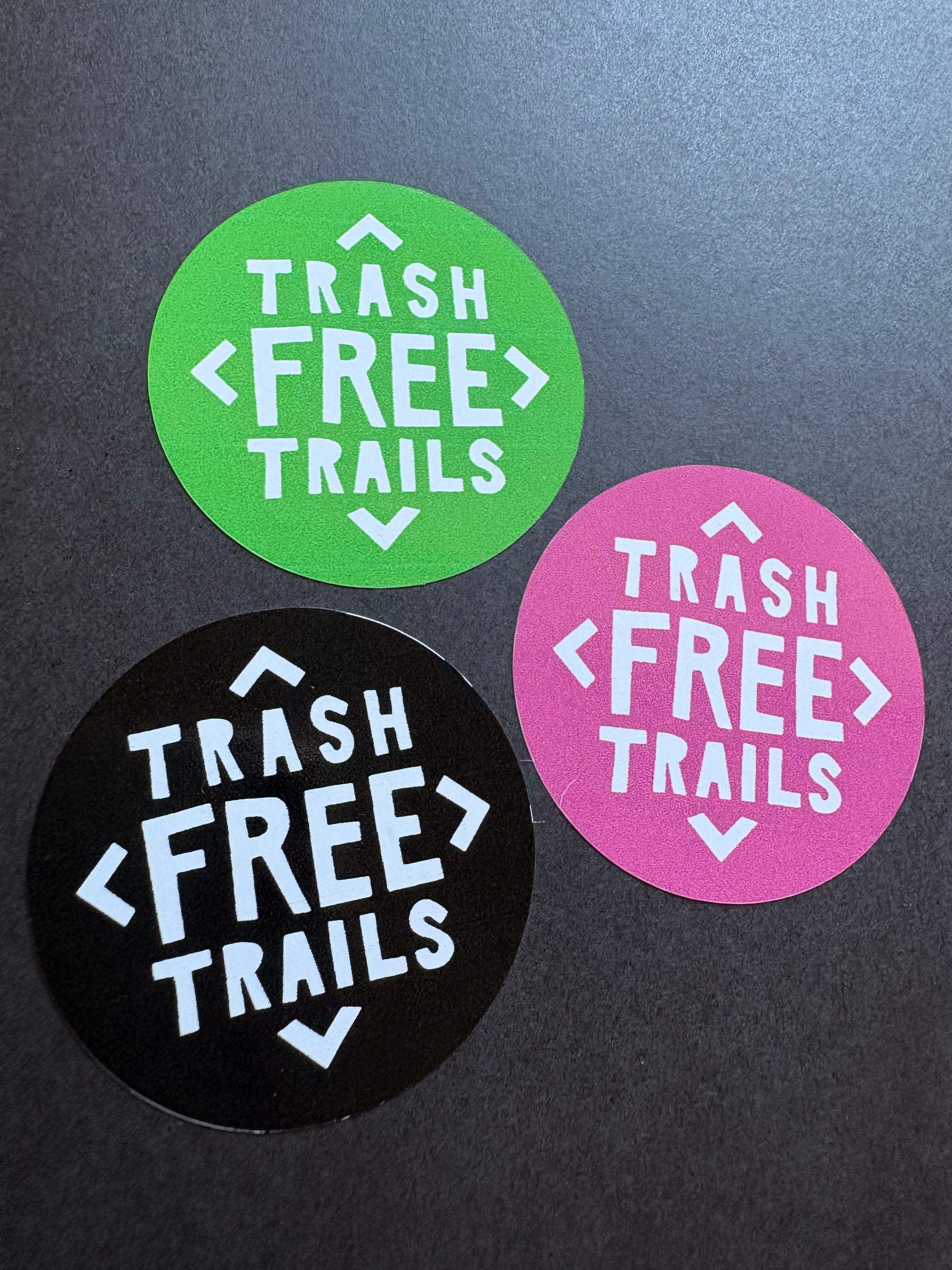 Three circular stickers with 'Trash Free Trails' text on a dark background