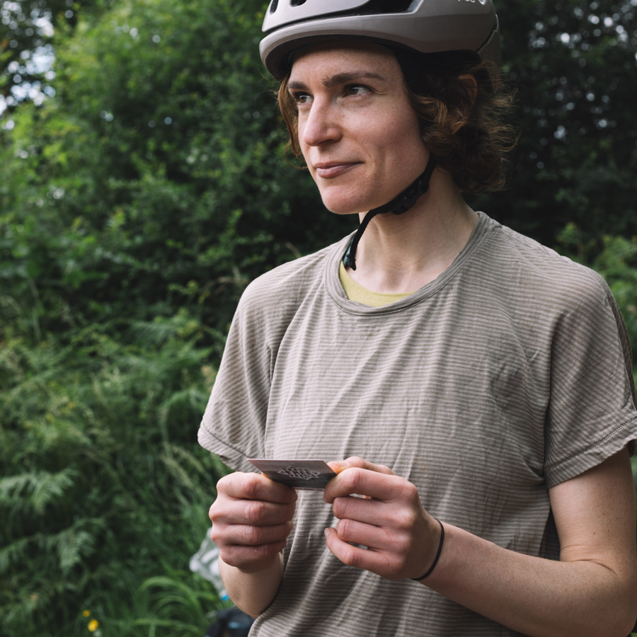 Person wearing a helmet and holding a phone outdoors with greenery in the background