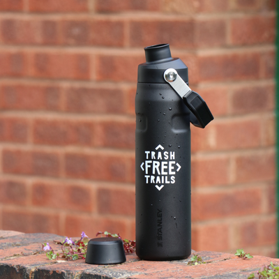 Trash Free Trails Black Bottle on a wall with the lid placed next to it.