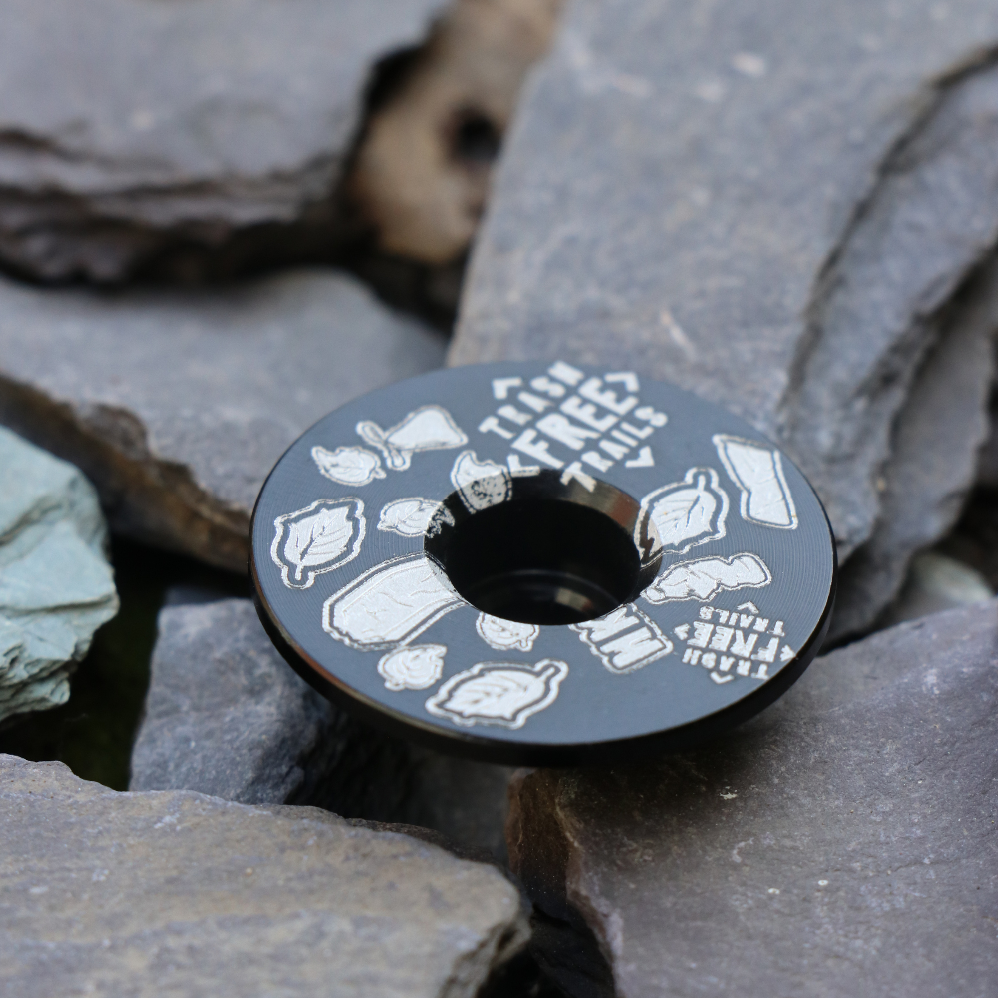 Trash Free Trails Black Stem Cap on grey stones.