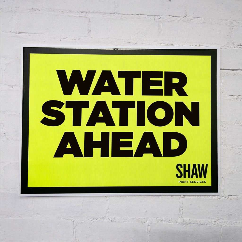 Framed sign with 'Water Station Ahead' text on a white brick wall