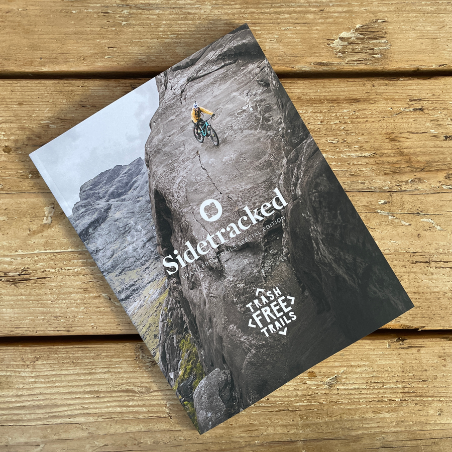 Trash Free Trails sidetracked magazine 2024 on a wooden background. The cover shows a bike rider on a mountain range. 